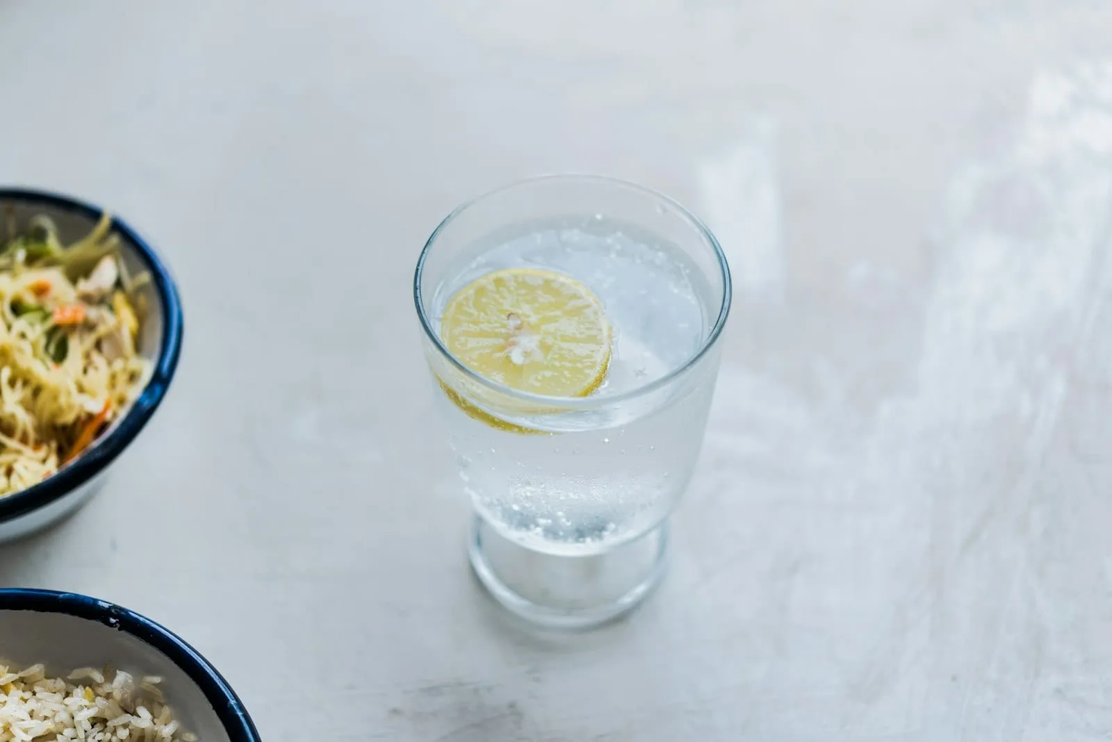 A glass of water with a slice of lemon on a light table